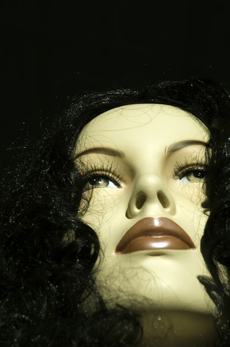 Face of female Caucasian mannequin wearing black wig in store window, sunset, close-up from below