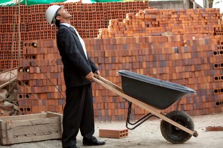 Elegant engineer with a wheel-barrow in a construction