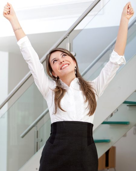 Friendly business woman full of success with her arms up at the office