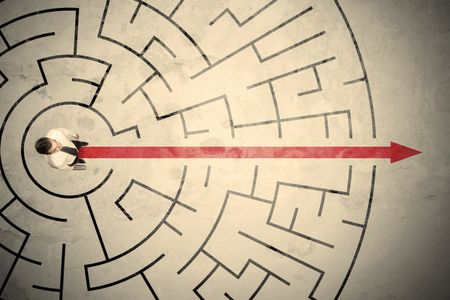 Business person standing in the middle of a circular maze with red arrow