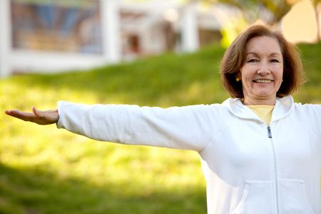Retired woman doing yoga exercises outdoors and smiling