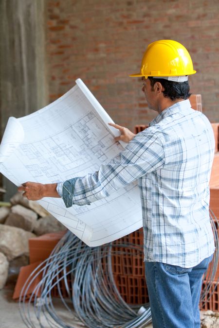 Male architect at a construction looking at blueprints