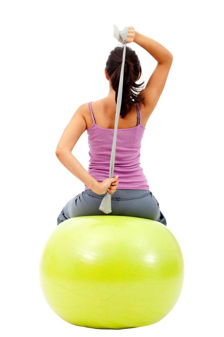Woman exercising on a pilates ball and stretching - isolated over white