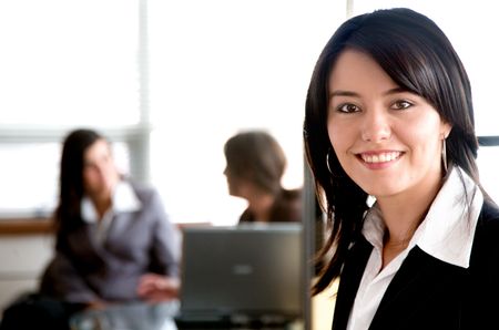 Business woman in an office with her team behind working on a laptop