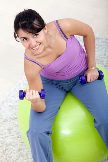 Woman exercising at home with weights and a pilates ball