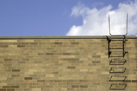 Iron rungs near end of exterior brick wall, a series of steps to roof and sky