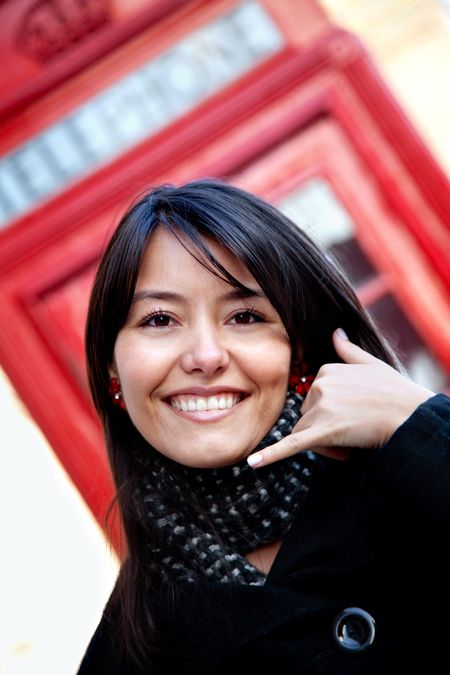 Woman standing in front of a telephone box doing a call me gesture