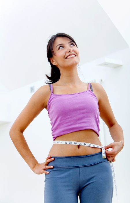 Beautiful fit woman measuring her waist and smiling