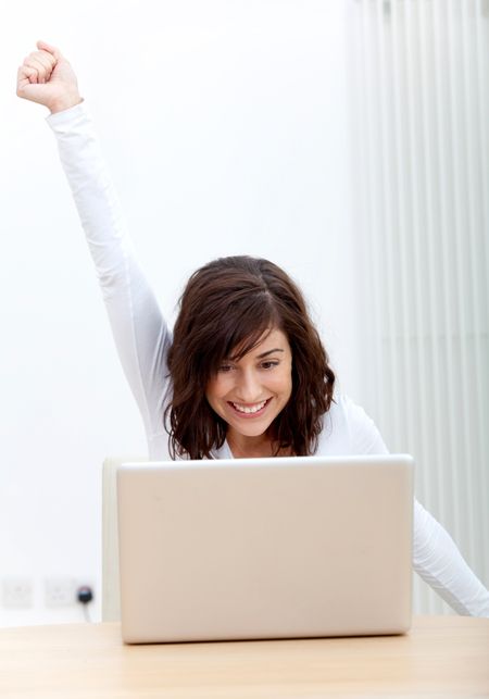 Happy woman working on a laptop with arms outstretched and smiling
