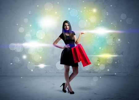 A beautiful young girl standing with long hair and red shopping bags in front of colorful light bokeh urban wall background concept