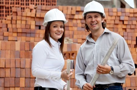 Engineers at a construction site holding blueprints and smiling