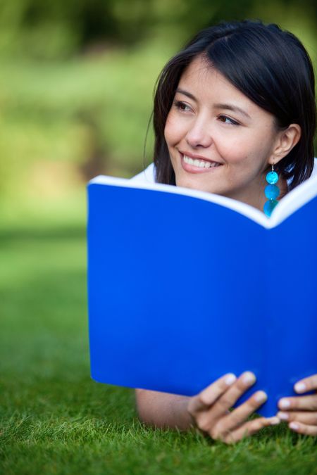 Beautiful female student with a notebook lying on the grass
