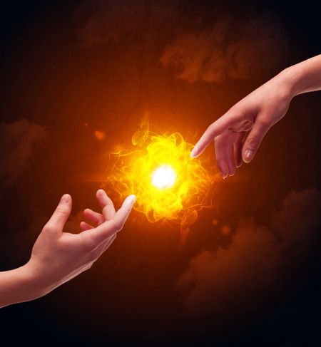 Two naked male hands about to touch, lighting a bright flame with smoke in red sky background concept