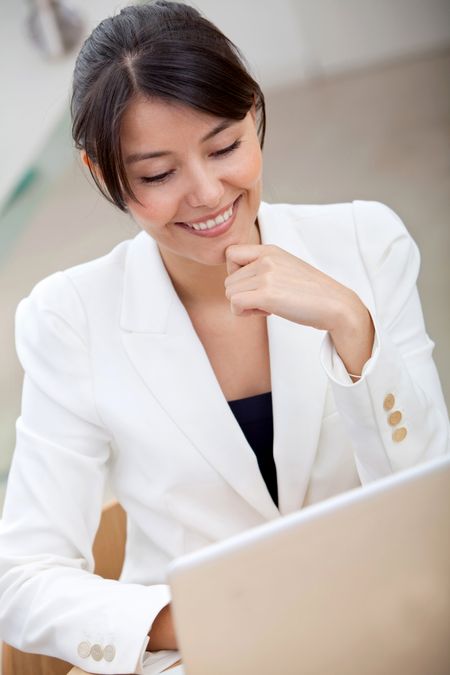 business woman looking happy on a laptop in her office