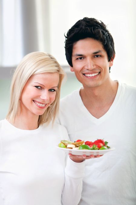 Healthy eating couple smiling and holding a dish of fruit