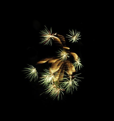 Group of similar fireworks bursts around feathery motion blur from previous explosion