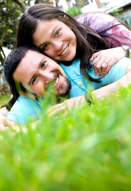 happy couple outdoors lying on the grass smiling at the camera