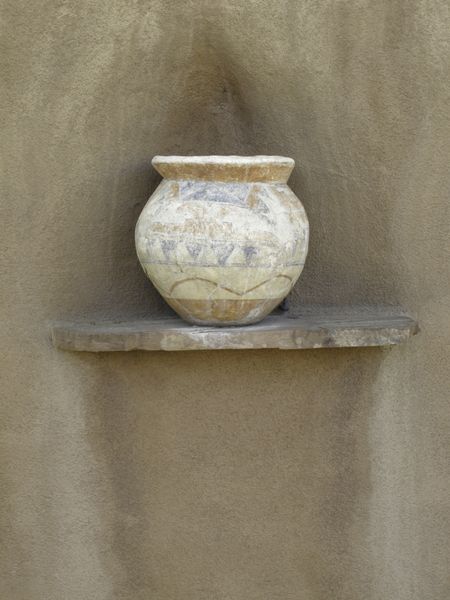 Ceramic pot with faded paint on ledge of exterior adobe wall
