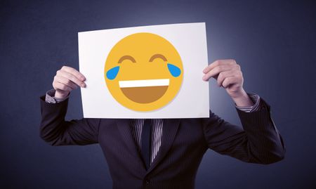 Young businessman hiding behind a laughing emoticon on cardboard