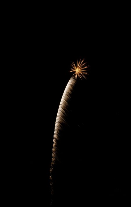 Feathery white rocket trail ending in small, reddish-orange burst of fireworks