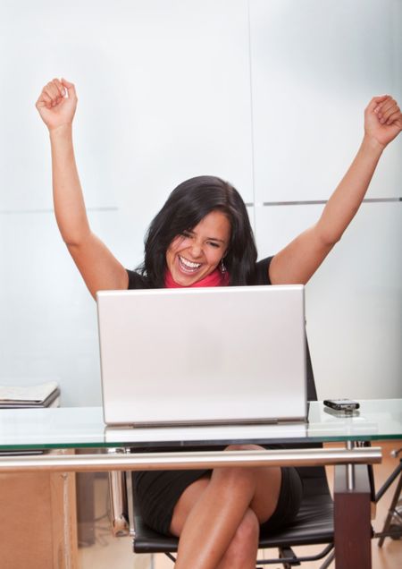 Successful business woman working on a laptop at the office looking excited