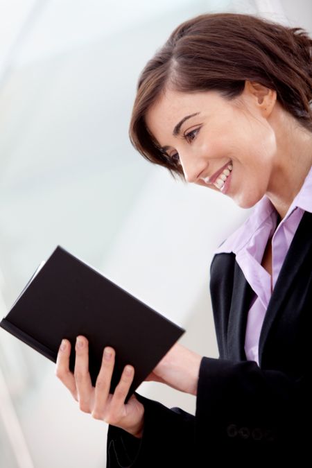 Business woman at the office reading a book and smiling