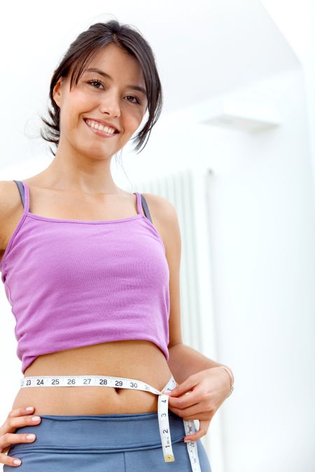Beautiful fitness woman in sportswear measuring her waist indoors