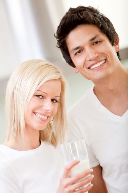 Happy couple holding a glass of milk and smiling - indoors