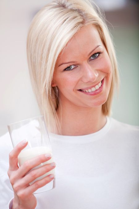 Woman holding a glass of milk and smiling ? indoors