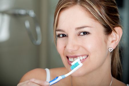 Woman with a toothbrush brushing her teeth and smiling