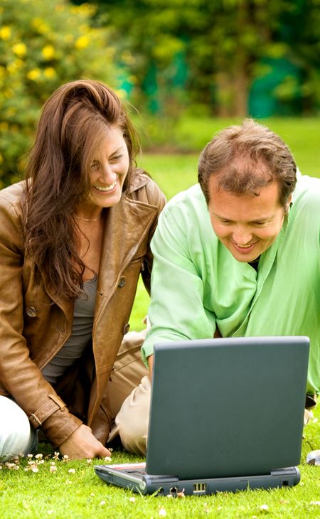 happy couple outdoors in a park looking happy while browsing the wireless web on a laptop