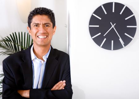 happy business man portrait in his office next to a clock