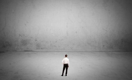 A tiny elegant businessman standing in large empty urban space with concrete walls and grey background concept