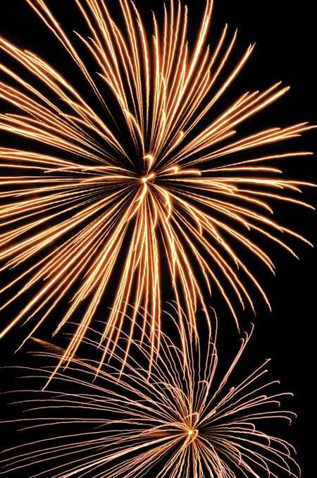 Two bursts of fireworks, the top reddish-yellow, the bottom silver with reddish-orange interior