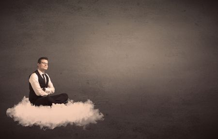 Caucasian businessman sitting on a white fluffy cloud wondering with a plain grunge background