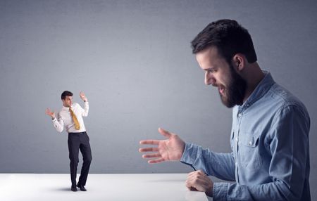 Young professional businessman being angry with an other miniature businessman in front of a grey background