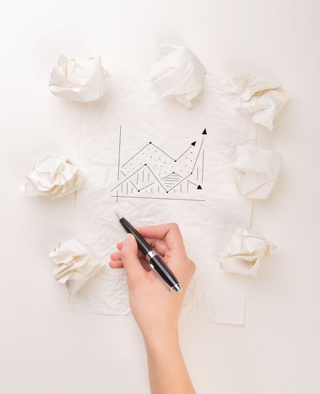 Female hand next to a few crumpled paper balls drawing a progress chart