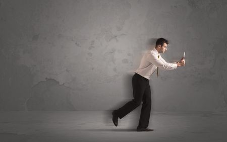 Running businessman in a rush with device in hand on background