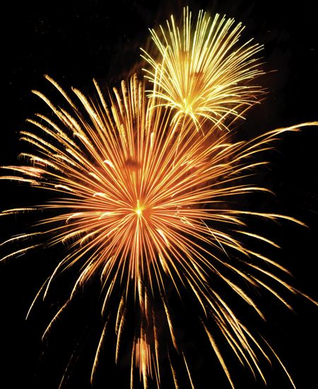 Two bursts of fireworks, the smaller yellow-white, the larger reddish-orange and yellow