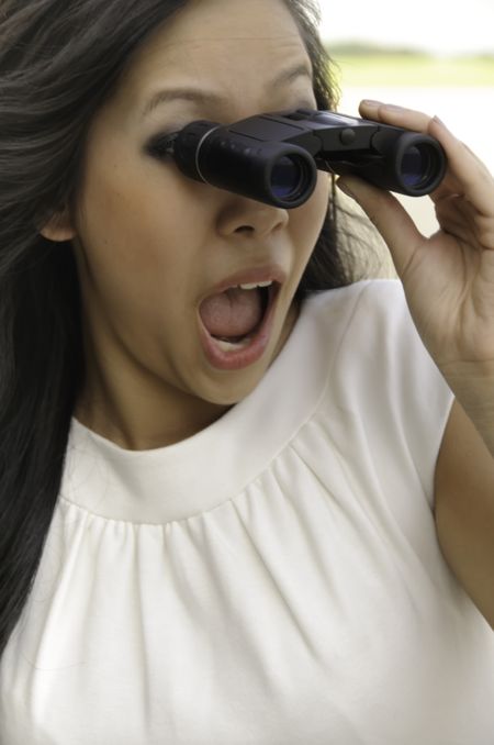 Young Asian-American woman looks surprised as she gazes through binoculars