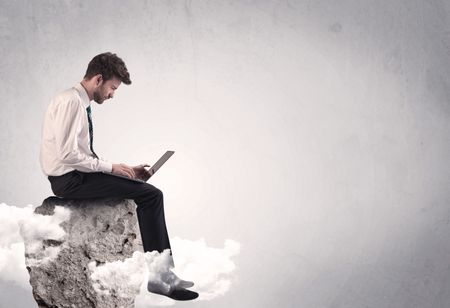 An elegant  smart businessman with laptop sitting in empty grey space on top of a cliff, between clouds concept