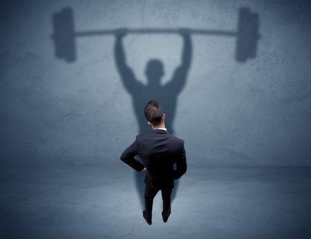 A confident young elegant salesman with briefcase facing a wall, looking at his strong, weight lifting shadow concept