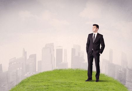 A confident male well looking office manager standing in small green grass in front of city landscape with tall buildings concept.