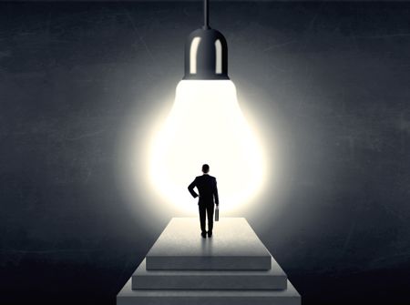 Businessman standing on a step in front of a huge light bulb, concept of having an idea.