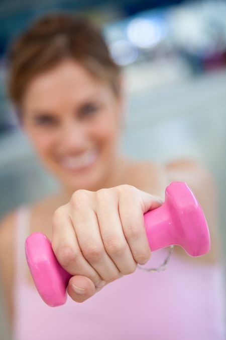 Blurry woman at the gym lifting a free-weight and smiling
