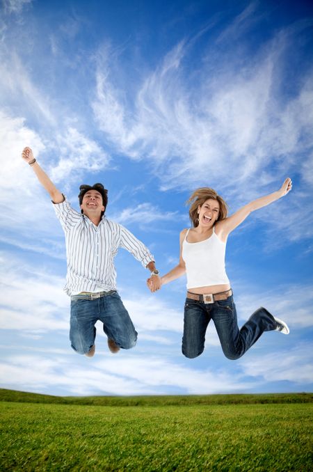 Excited couple holding hands and jumping outdoors