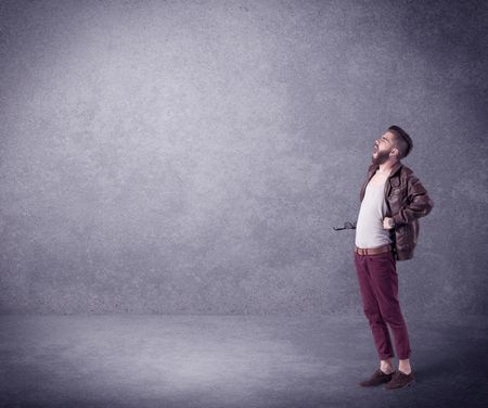 A hipster guy in stylish clothes shouting in front of an empty urban concrete wall background concept