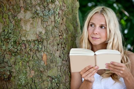 Beautiful woman reading a book outdoors under a tree