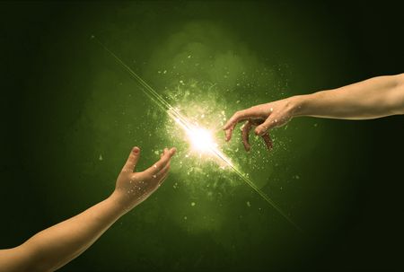 Two naked male hands about to touch, lighting the spark with modest explosion in front of green background concept