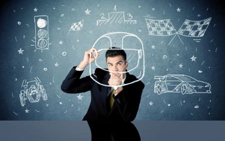 A happy businessman sitting at desk and drawing race car, flag, helmet around himself with a white chalk concept